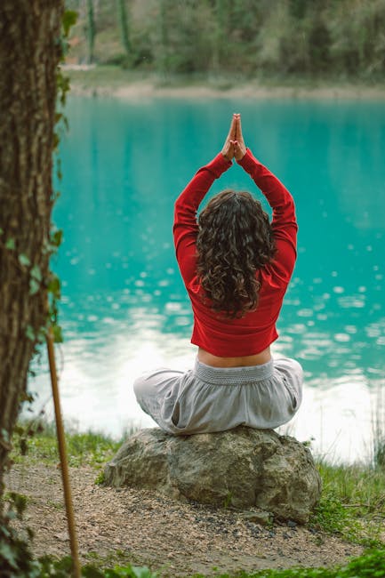 A woman in a red blouse meditates with arms raised by a tranquil lake, creating a serene scene.
